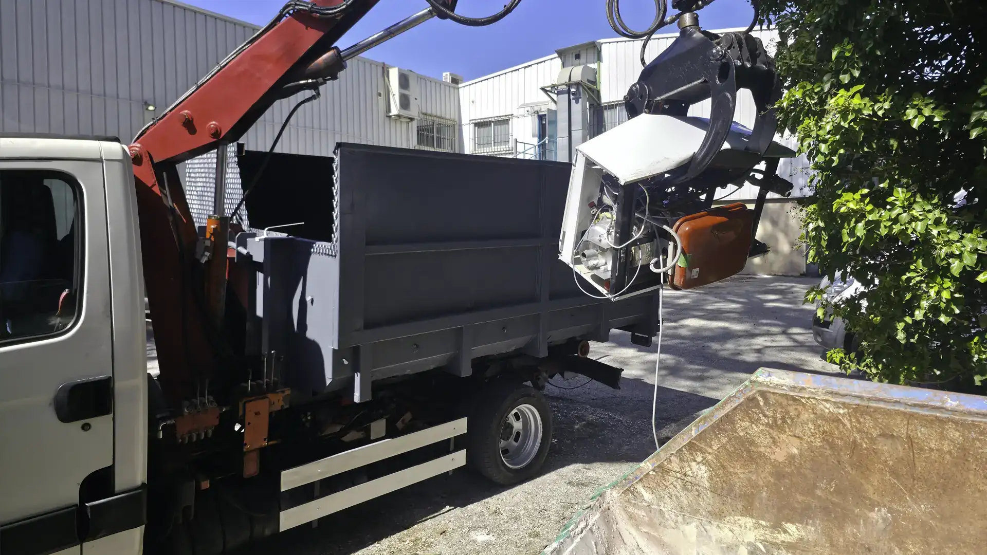 Le camion grue de RJ Benne : le grappin soulève une vieille chaudière au-dessus de la benne du camion, une benne de chantier au premier plan.