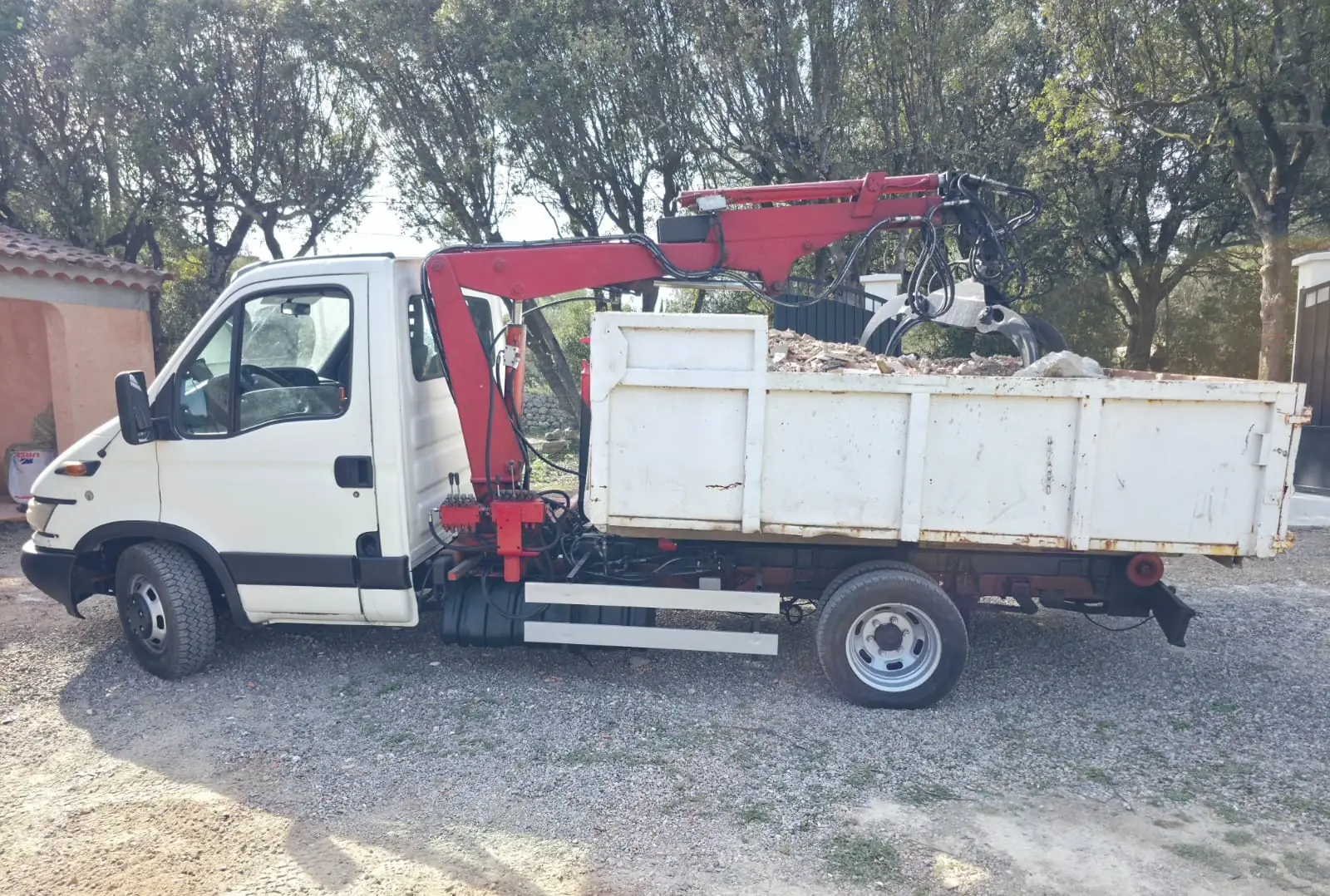 Le camion de RJ Benne de profil : sa benne blanche pleine de gravats (briques, tuiles, béton), le grappin posé sur le chargement.