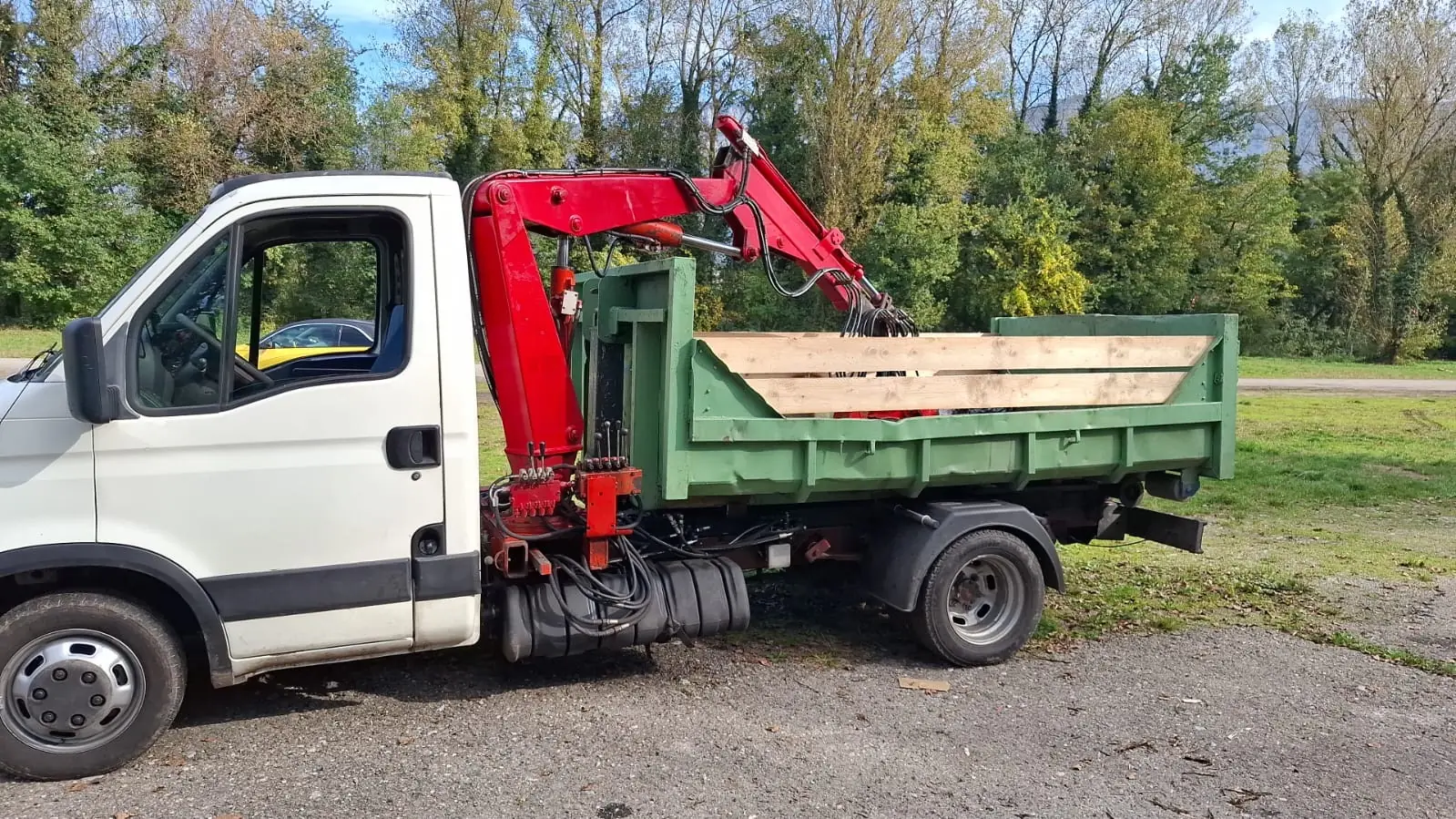 Le camion de RJ Benne de profil, sa benne verte chargée de planches, le grappin replié sur le chargement.